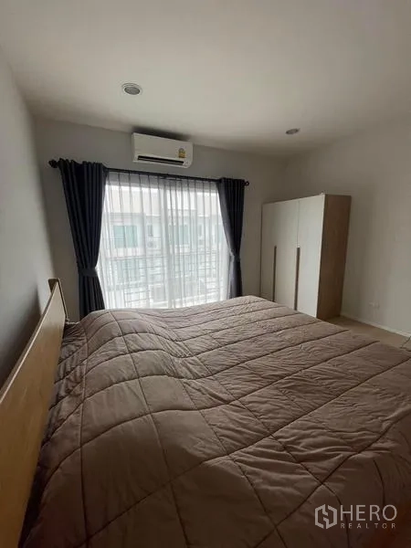 Townhouse for rent in Suan Luang, Bangkok - Guest bedroom with large bed, freestanding wardrobe and balcony window with drapes.