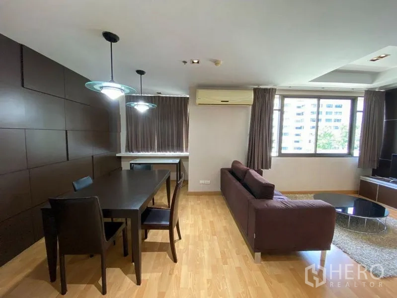 Condominium for rent in Khlong Toei, Bangkok - Open-plan living and dining area with wood floors, pendant lights, and large windows in a Sukhumvit condo.