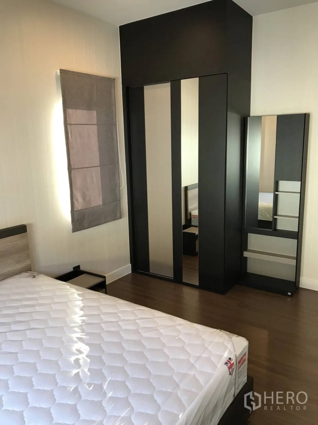 Detached House for rent in Bang Kapi, Bangkok - Bedroom with dark built-in wardrobe, mirror panels and bedside table on timber floor.