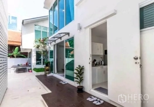 Townhouse for rent in Khlong Toei, Bangkok - Side walkway and entrance with sliding glass doors and a compact kitchen visible inside.