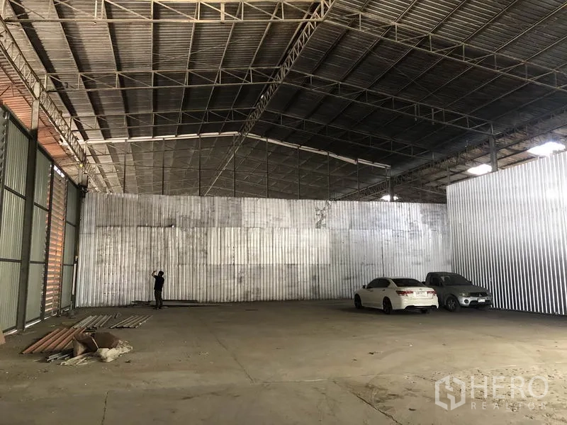 Warehouse for rent in Nong Chok, Bangkok - Open warehouse bay with corrugated metal walls, concrete flooring, and parking space for cars under a steel roof.