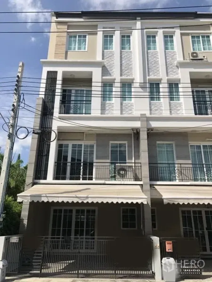 Townhouse for rent in Bang Na, Bangkok - Modern multi‑level townhouse facade with balconies, awnings, and a gated entrance in Bang Na.