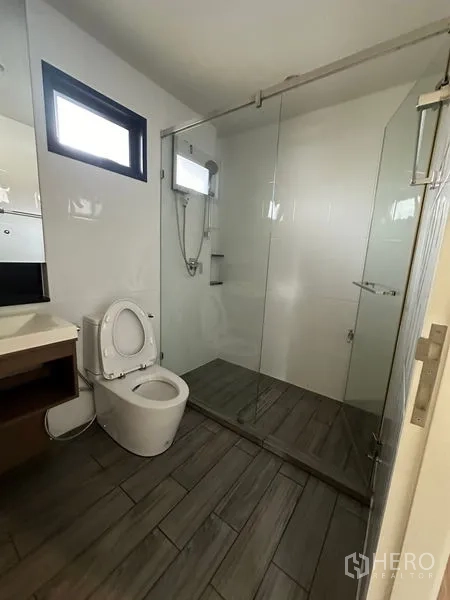 Detached House for rent or sale in Lam Luk Ka, Pathum Thani - Bathroom featuring a glass-enclosed shower, white walls and gray plank flooring.