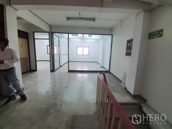 Shophouse for rent in Bang Rak, Bangkok - Corridor with exit sign, staircase rail and a large glass-walled room in a commercial shophouse.