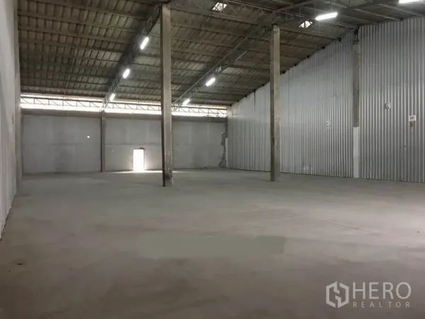 Warehouse for rent in Bang Phli, Samut Prakan - Spacious empty warehouse interior with high roof, bright strip lighting, corrugated side wall and smooth concrete floor.