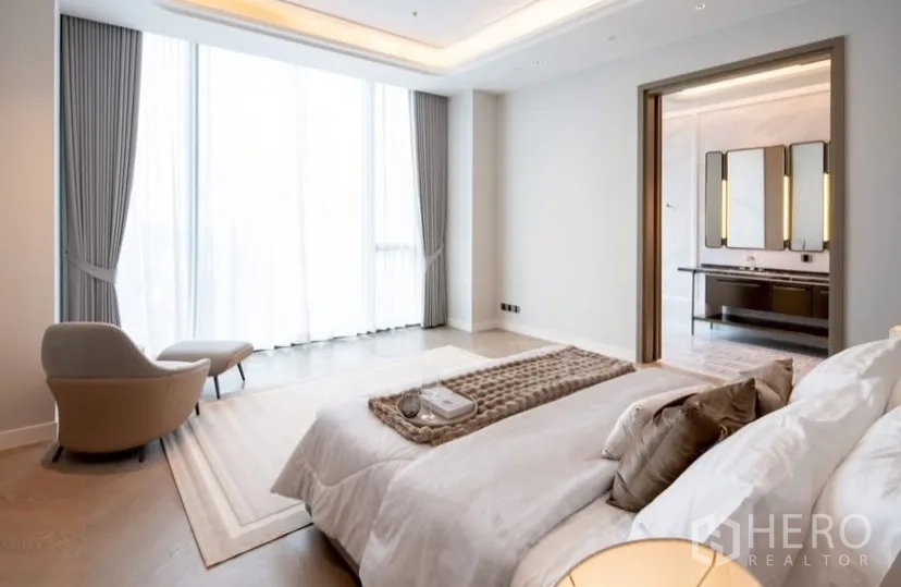 Condominium for rent or sale in Pathum Wan, Bangkok - Primary suite showing large windows with sheer curtains and the entrance to a marble bathroom.