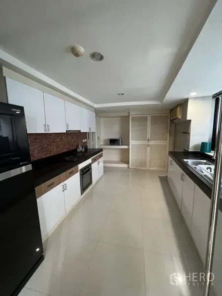 Condominium for rent - Long galley kitchen with white cabinetry, black countertops, oven and full-size fridge.