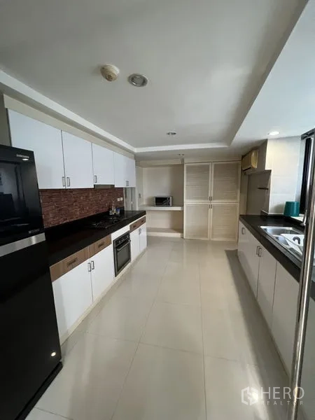Condominium for rent - Long galley kitchen with white cabinetry, black countertops, oven and full-size fridge.