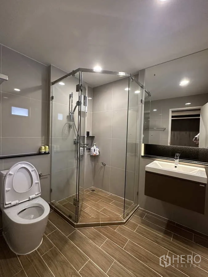 Detached House for rent or sale in Lam Luk Ka, Pathum Thani - Modern bathroom with glass shower enclosure, wall‑hung vanity and tiled floor.