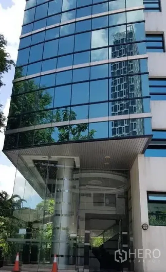 Office Space for rent in Khlong Toei, Bangkok - Glass curtain-wall entrance of an office building reflecting the skyline, with canopy and columns.