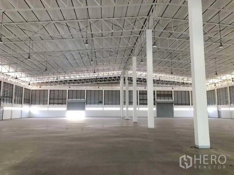 Factory for rent or sale in Phra Nakhon Si Ayutthaya - Vast production hall with high steel truss roof, white columns and smooth concrete floor.