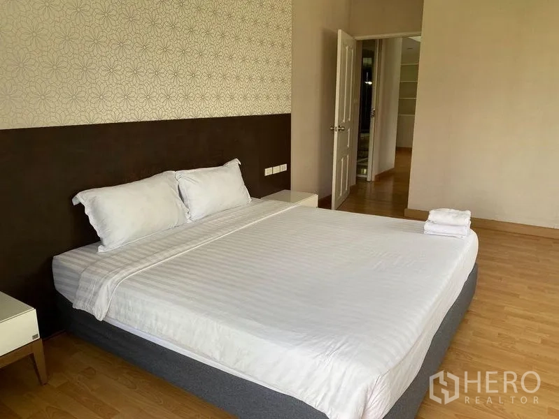 Condominium for rent in Khlong Toei, Bangkok - Bedroom angle showing feature wall, bedside tables, and doorway to the living area.