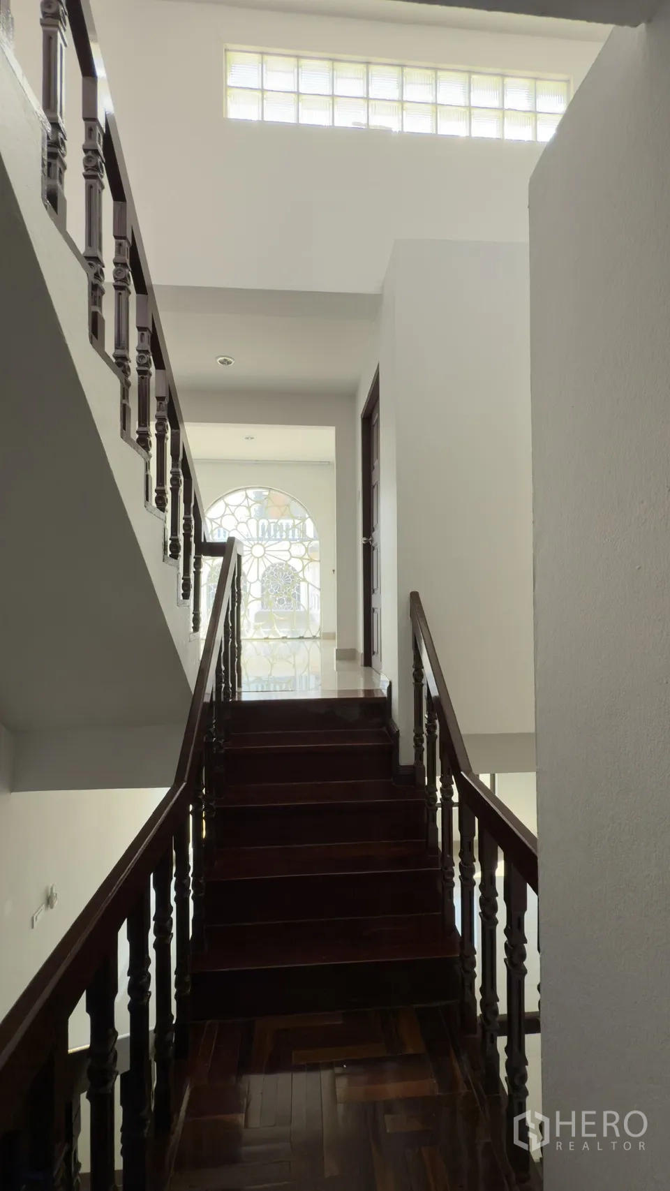 Townhouse for rent in Watthana, Bangkok - Stairwell with wooden steps, a glass-block skylight, and an arched decorative window.