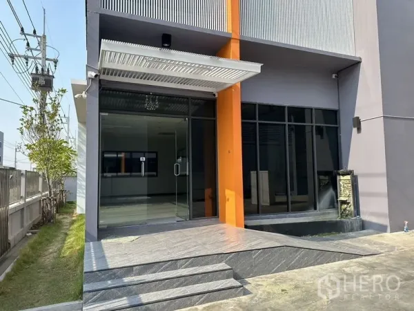 Factory for rent or sale in Lam Luk Ka, Pathum Thani - Close-up of the main entrance with glass doors, canopy and steps at the office building.