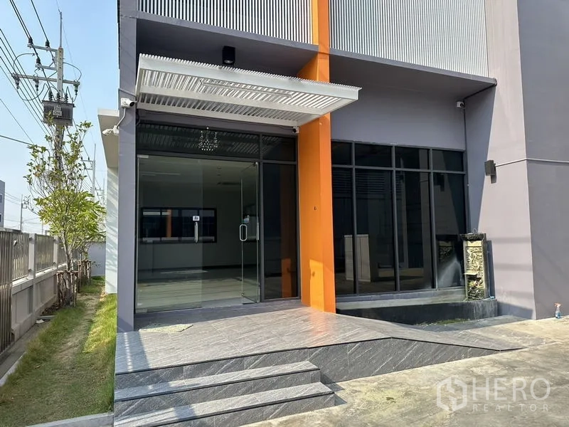 Factory for rent or sale in Lam Luk Ka, Pathum Thani - Close-up of the main entrance with glass doors, canopy and steps at the office building.