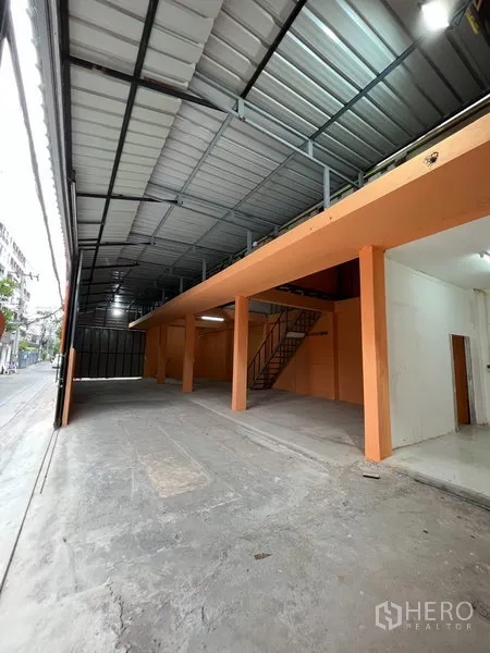 Warehouse for rent in Din Daeng, Bangkok - Open-plan warehouse interior with high metal roof, orange columns, mezzanine level and concrete floor with direct street access.