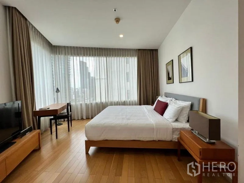 Condominium for rent in Khlong Toei, Bangkok - Spacious master bedroom with large windows, city view, desk and a queen bed with neutral decor.