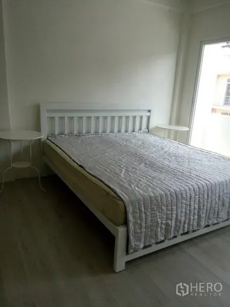 Townhouse for sale in Khlong Toei, Bangkok - Simple bedroom with white bed frame, large window, and light wood flooring.