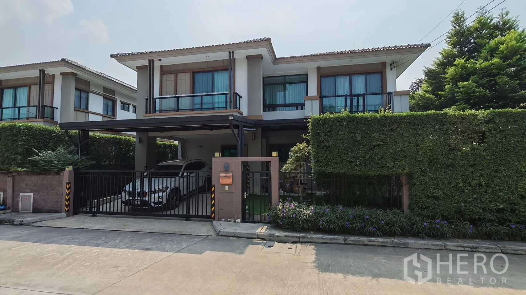 Detached House for rent or sale in Bang Phli, Samut Prakan - Front facade with gated entrance, covered two‑car carport, and landscaped hedges.