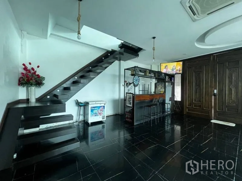Detached House for sale in Lat Phrao, Bangkok - Hall with bar counter, floating stairs, and grand carved wooden entrance door.