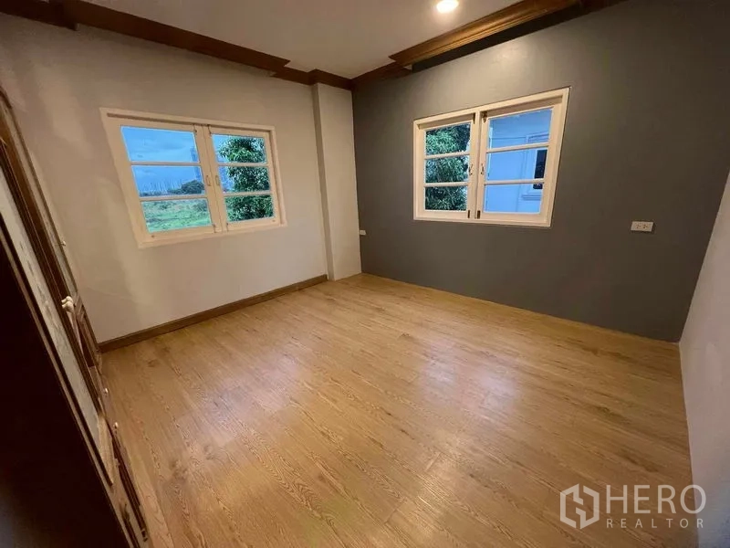 Detached House for sale in Bang Na, Bangkok - Corner bedroom with light wood flooring, twin windows and a grey feature wall.