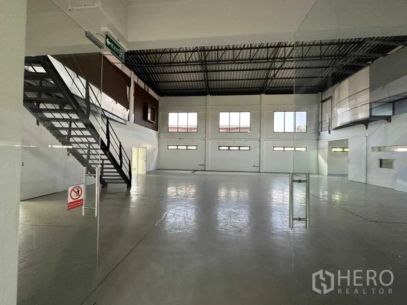 Warehouse for rent in Phra Khanong, Bangkok - Ground-floor storage area with steel staircase and smooth concrete flooring.