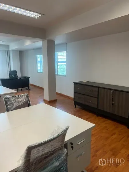 Office Space for rent in Khlong Toei, Bangkok - Bright office area with a manager’s desk by the windows and a low storage cabinet on wood flooring.