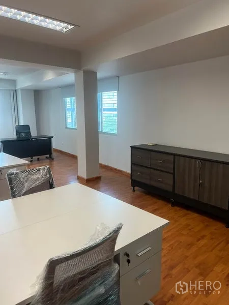 Office Space for rent in Khlong Toei, Bangkok - Bright office area with a manager’s desk by the windows and a low storage cabinet on wood flooring.