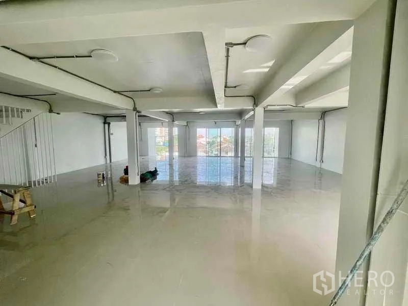Home Office for rent or sale in Bang Kapi, Bangkok - Large ground‑floor hall with polished floors, structural columns, staircase, and floor‑to‑ceiling windows.