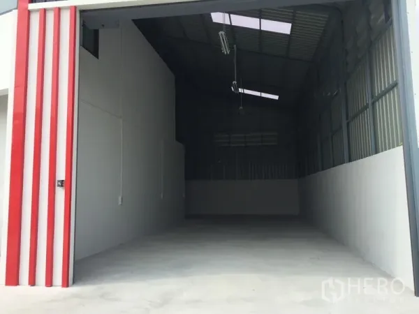 Warehouse for sale in Khlong Luang, Pathum Thani - Large roller shutter entrance with red trim opening to a spacious warehouse.