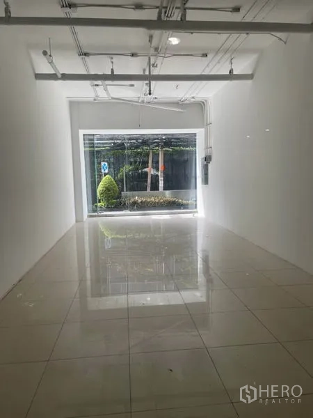 Retail Space for rent in Khlong Toei, Bangkok - Bright white-box interior with tiled flooring, high ceiling and exposed track lighting facing a large window.