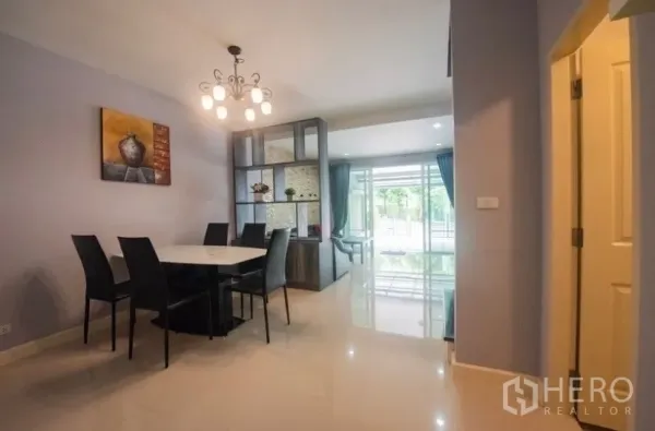 Townhouse for rent in Suan Luang, Bangkok - Dining zone with modern chandelier, four-seat table and shelving divider beside wide sliding glass doors.