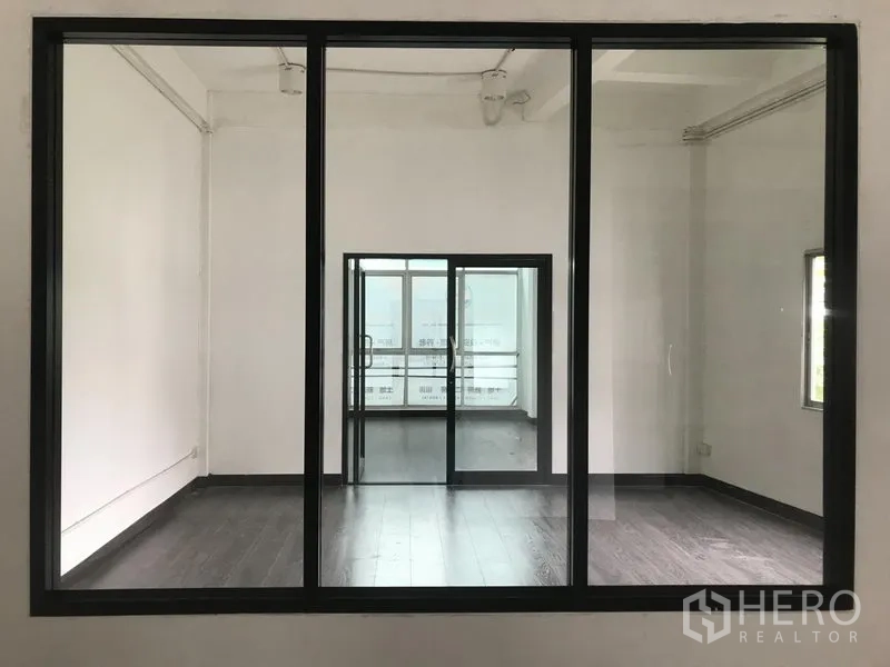 Shophouse for rent in Watthana, Bangkok - Black-framed interior window looking into two connected rooms with natural light.