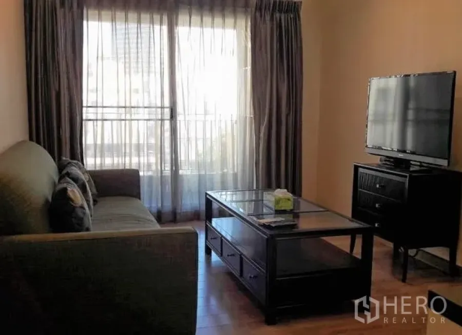Condominium for rent in Pathum Wan, Bangkok - Bright living room with large window, sheer curtains, TV console and a glass coffee table on wood flooring.