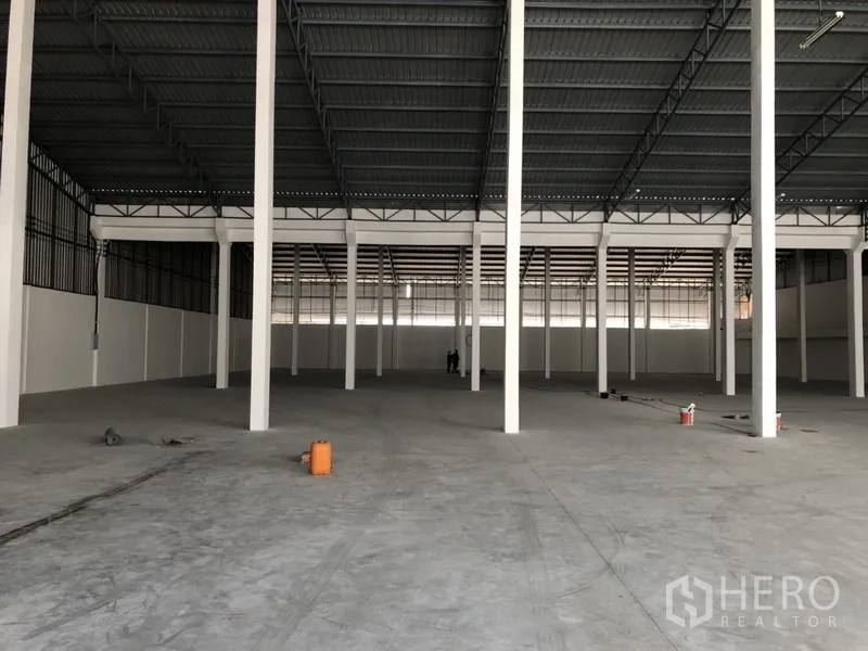 Warehouse for rent in Nonthaburi - Spacious warehouse interior with high steel truss roof, white columns, and reinforced concrete floor.