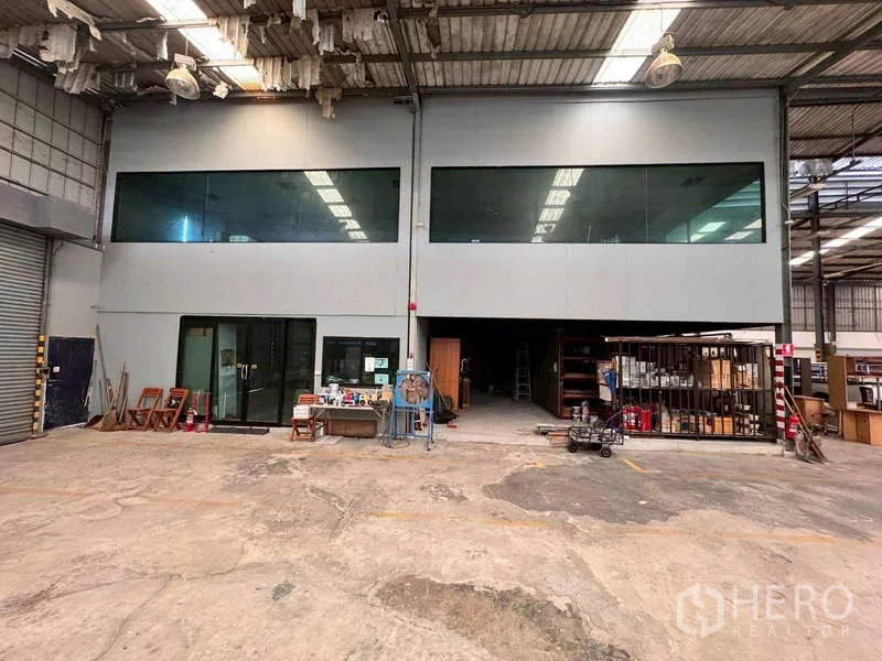 Warehouse for rent in Prawet, Bangkok - Spacious warehouse interior with mezzanine glass-walled office and concrete floor.