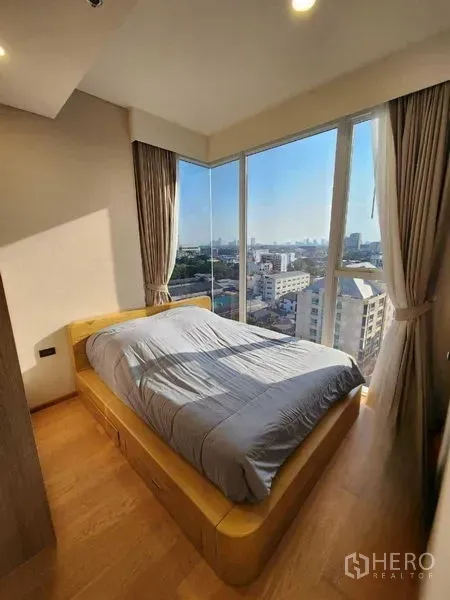 Condominium for rent in Khlong Toei, Bangkok - Bright master bedroom with floor-to-ceiling corner windows and city view.