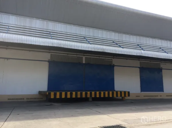 Warehouse for rent in Lat Krabang, Bangkok - Exterior of a Lat Krabang warehouse featuring a covered loading dock, ventilation awnings and blue sliding doors.