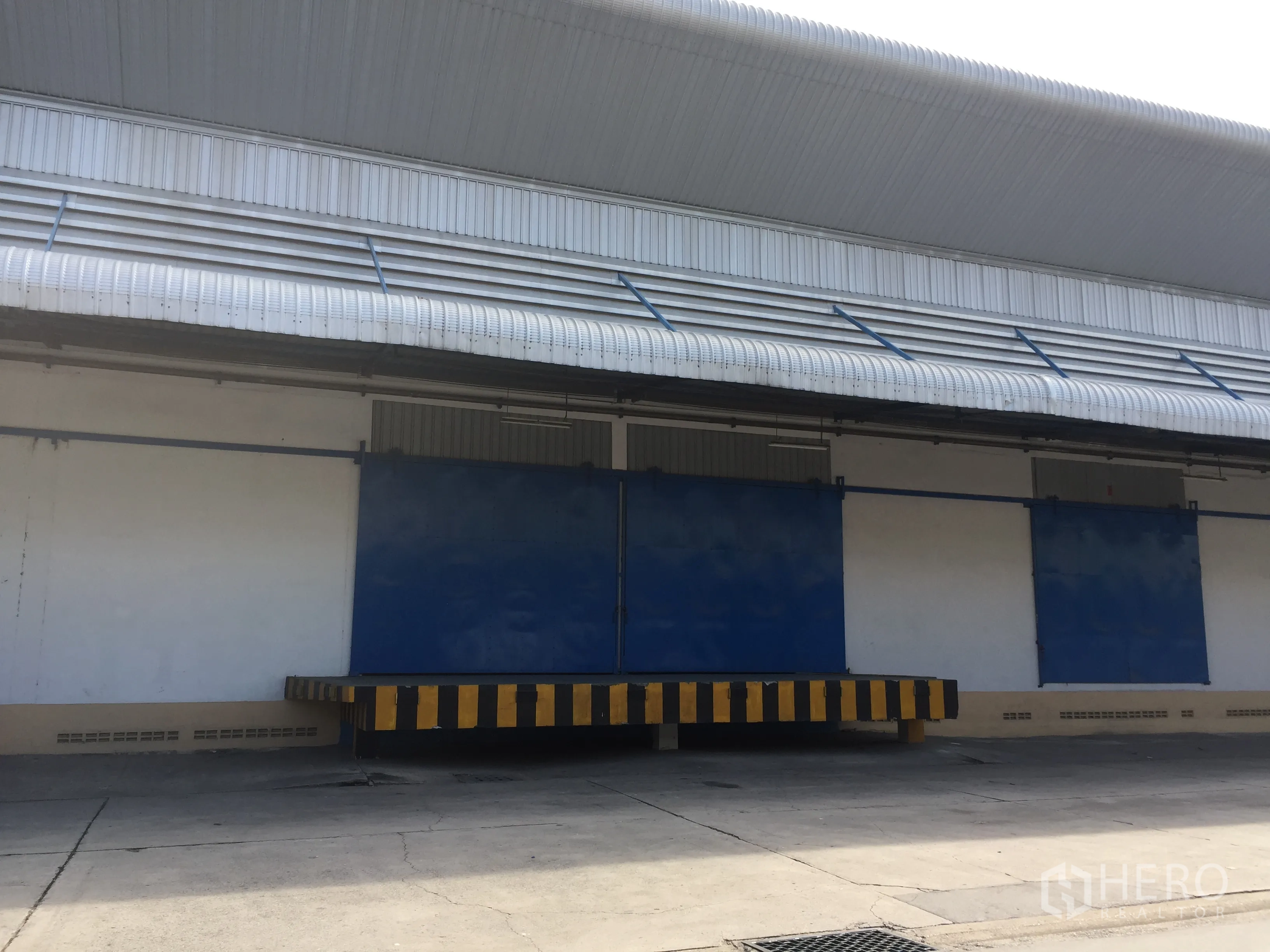 Warehouse for rent in Lat Krabang, Bangkok - Exterior of a Lat Krabang warehouse featuring a covered loading dock, ventilation awnings and blue sliding doors.