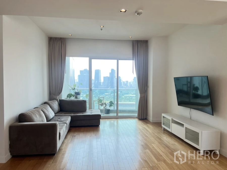 Condominium for sale in Khlong Toei, Bangkok - Living room with L-shaped sofa, balcony doors and far-reaching city and park views.