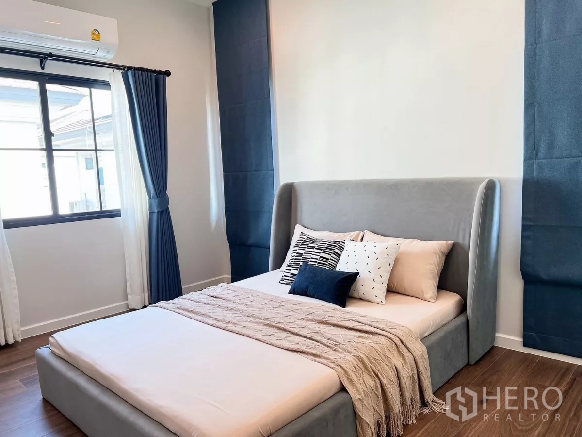 Detached House for rent in Khan Na Yao, Bangkok - Sunlit bedroom with gray bed, blue curtains and window overlooking the neighborhood.