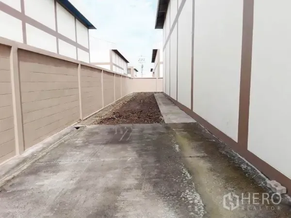 Factory for sale in Pathum Thani - Side service lane and utility strip along the factory boundary wall.