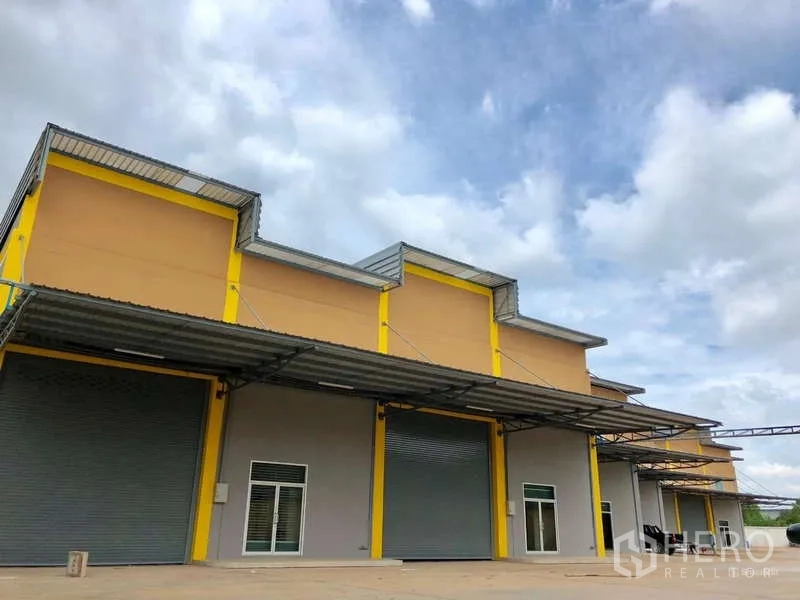 Factory for rent in Mueang Samut Sakhon, Samut Sakhon - Modern factory exterior with yellow accents, large roller shutter doors, and covered loading bays.