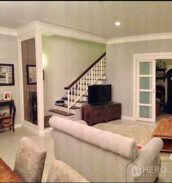 Townhouse for rent or sale in Bangkok - Living area with staircase, TV console, soft-toned walls and sliding glass doors.