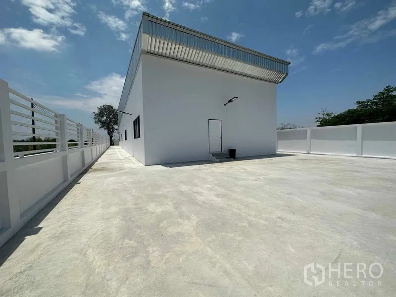 Warehouse for sale in Khlong Luang, Pathum Thani - Rear concrete yard surrounding the white warehouse with a side service door.