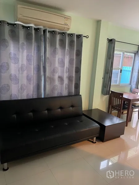 Townhouse for rent in Khlong Toei, Bangkok - Bright living area with black sofa, tiled floor, curtains, air conditioner and dining nook