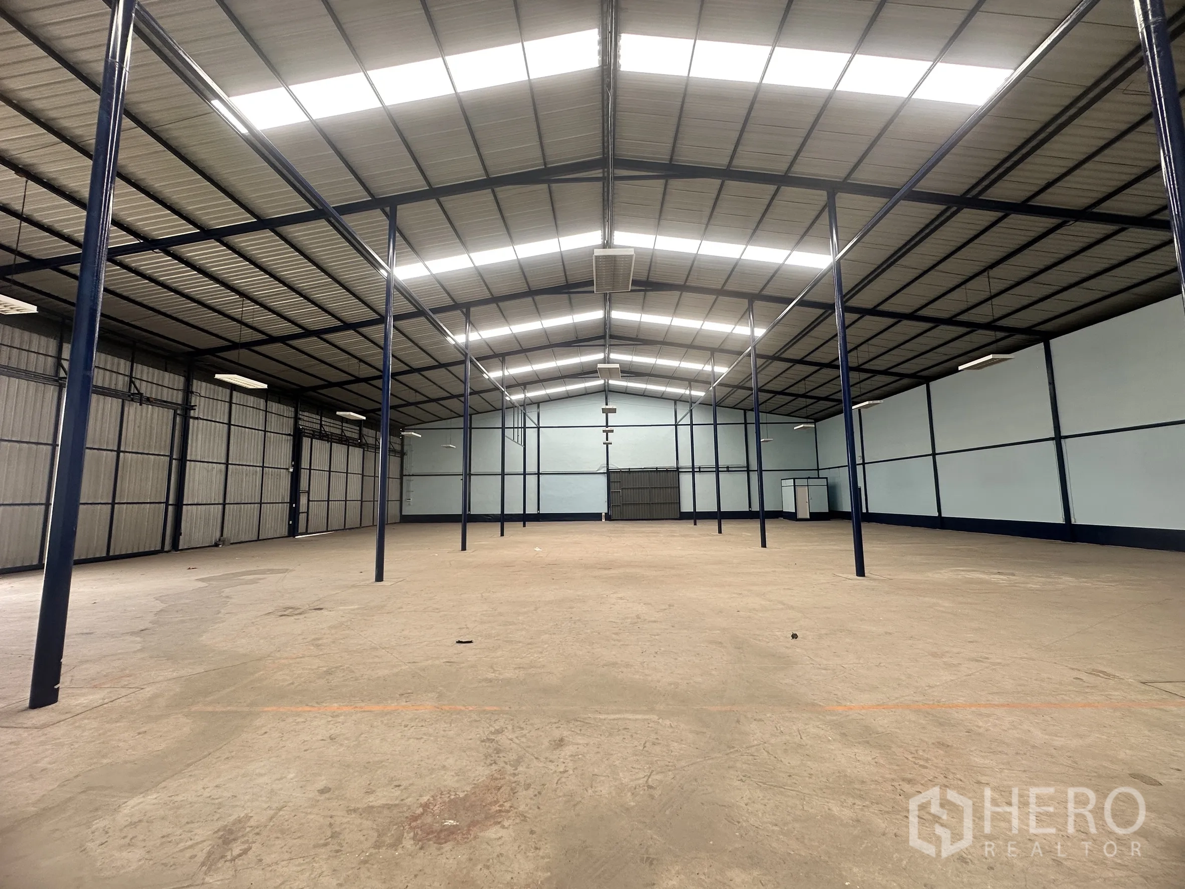 Warehouse for rent in Lat Krabang, Bangkok - Spacious storage hall with steel columns, overhead lights, and shuttered side wall.