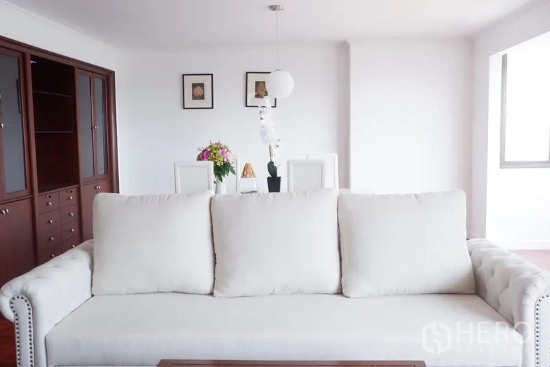 Condominium for rent in Khlong Toei, Bangkok - Cream sofa facing dining area with dark wood cabinetry in a bright room.