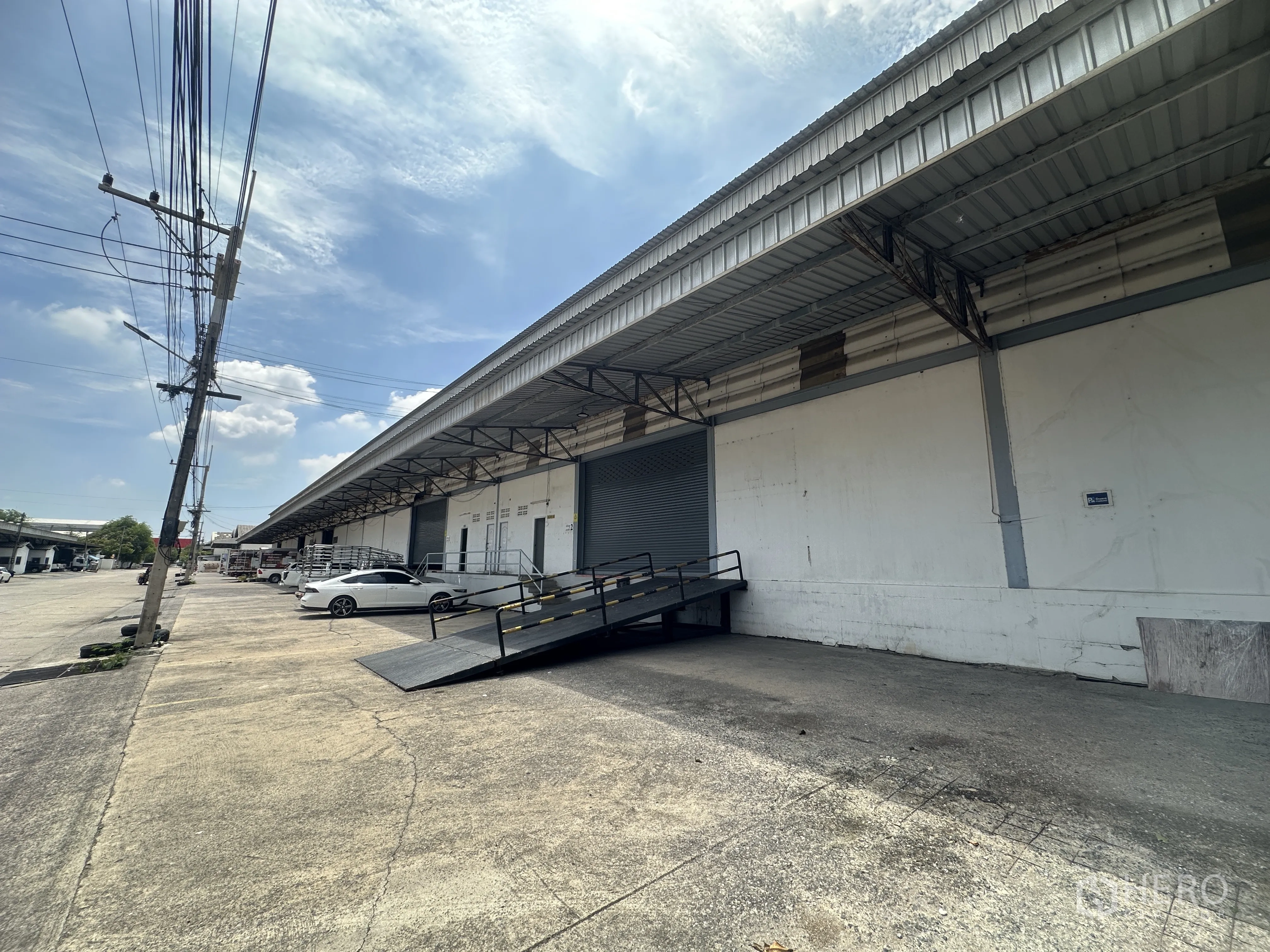 Warehouse for rent in Khlong Luang, Pathum Thani - Exterior loading dock with covered canopy, metal ramp, and parking area.