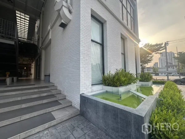 Retail Space for rent in Khlong Toei, Bangkok - Building corner with landscaped water feature, steps and city backdrop at sunset.